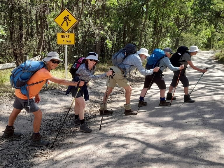 five bushwalkers mimic the road sign that says walkers are likely for the next kilometre