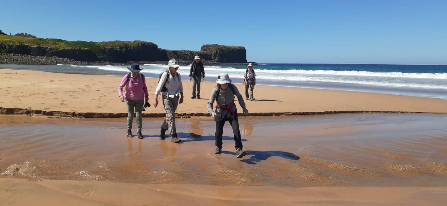 5 people crossing a creek inlet on a beach in Mimosa Rocks National Park